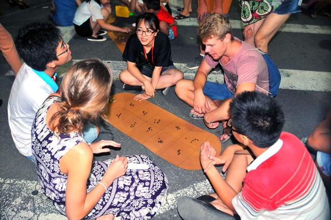 Иностранные туристы с вьетнамскими детьми участвуют в народной игре «О ан куан»